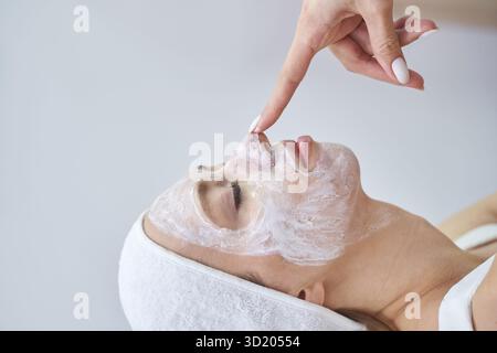 Giovane donna caucasica che riceve un trattamento viso con maschera di crema ringiovanente Foto Stock