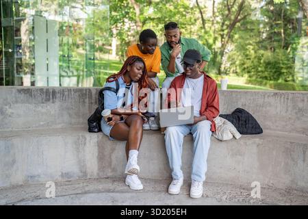 Gli amici studenti di colore lavorano su un computer portatile alla panchina del parco. Collaborazione progettuale, freelance, incontro di startup Foto Stock