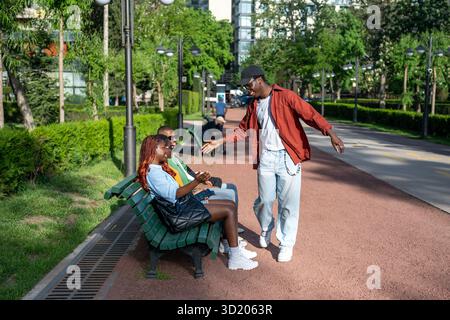 Un gruppo di amici neri si riunisce al parco durante il fine settimana. I giovani uomini condividono i fiocchi alti e si ritrovano Foto Stock