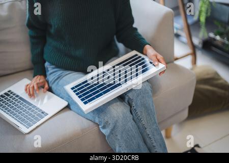 Donna asiatica che impara a conoscere le energie rinnovabili il controllo remoto dell'energia solare nella sua casa e l'installazione di pannelli solari sostenibili technolo Foto Stock