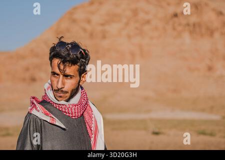 Ritratto di un giovane beduino che indossa una sciarpa rossa di keffiyeh alla luce del deserto di Wadi Rum, in Giordania. Foto Stock