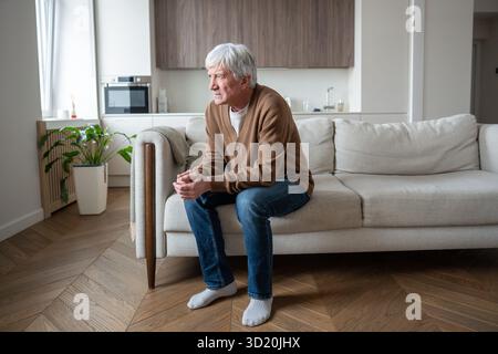 Un pensionato solitario e depresso siede con le braccia incrociate sul divano abbandonato dalla famiglia dopo la perdita di lavoro Foto Stock