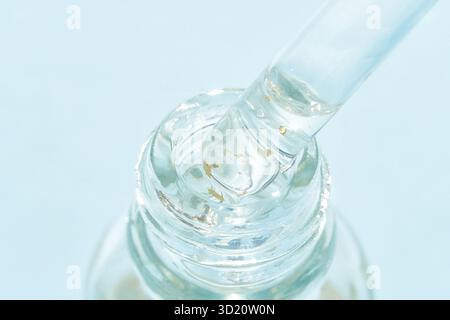 Primo piano di siero trasparente con scaglie d'oro nel flacone di vetro e contagocce acceso alla luce Foto Stock