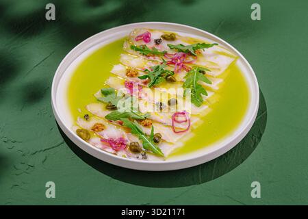 Il ceviche servito su un piatto bianco presenta pesce fresco con contorno vivace e salsa verde su uno sfondo verde suggestivo Foto Stock