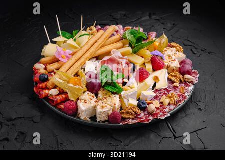 Squisito vassoio di salumi con una varietà di formaggi, carni, frutta e noci esposti elegantemente per un incontro di festa Foto Stock