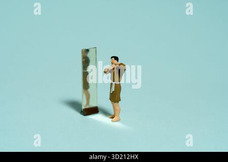 Fotografia di figure giocattolo in miniatura. Un uomo che indossa un accappatoio si radica la barba davanti allo specchio. Isolato su sfondo verde. Immagine Foto Stock