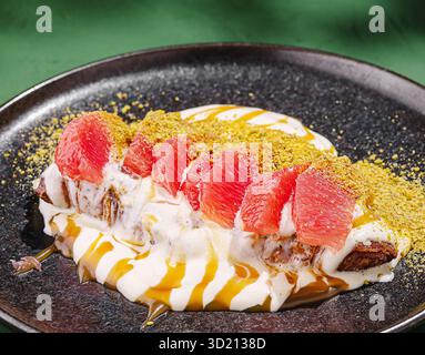 Dessert saporito con strati di cremoso yogurt, frutta e noci presentati su un piatto scuro in un ambiente vivace Foto Stock