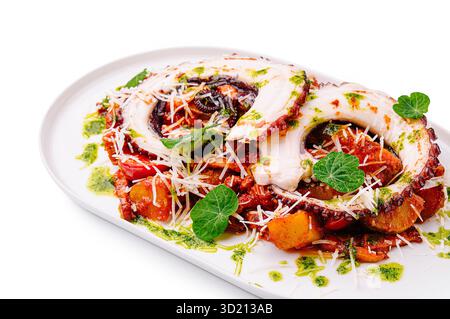 Tentacoli di polpo grigliato serviti con verdure arrostite ed erbe su un piatto bianco Foto Stock