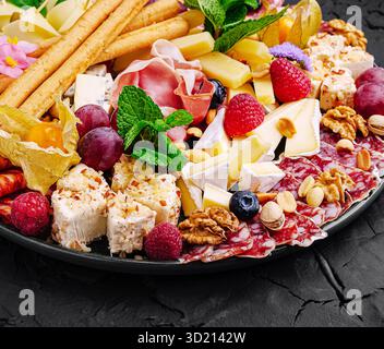 Squisito vassoio di salumi con una varietà di formaggi, carni, frutta e noci esposti elegantemente per un incontro di festa Foto Stock