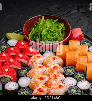 Delizioso piatto di sushi con vari rotoli e lati su una superficie scura Foto Stock