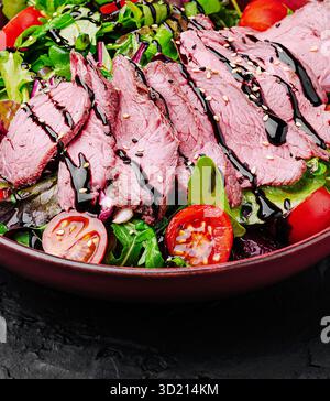 Insalata fresca con manzo arrosto, pomodori ciliegini e germogli balsamici su fondo di pietra scura Foto Stock