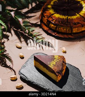 Deliziosa fetta di torta a strati servita su una tavola rustica di ardesia nera con foglie verdi decorative in luce naturale Foto Stock