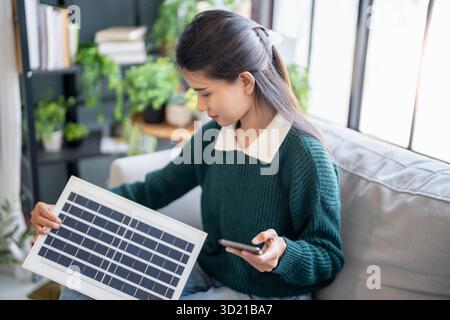 Donna asiatica che impara a conoscere le energie rinnovabili il controllo remoto dell'energia solare nella sua casa e l'installazione di pannelli solari sostenibili technolo Foto Stock