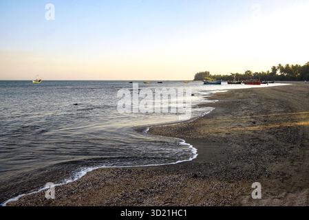 Tranquilla spiaggia con barche e onde dolci al tramonto Foto Stock
