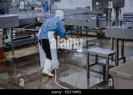 Fabbrica silenziosa, pochi operai che puliscono la linea di produzione trasportano il nastro si preparano a chiudere la fabbrica di alimenti Foto Stock