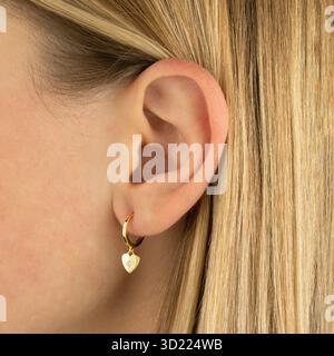 Elegante orecchino a cuore dorato sull'orecchio della giovane donna caucasica Foto Stock
