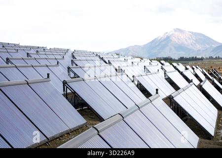 Pannelli solari in campo contro montagne lontane innevate. Apparecchiature di generazione di energia rinnovabile nell'altopiano. Sustainabl Foto Stock