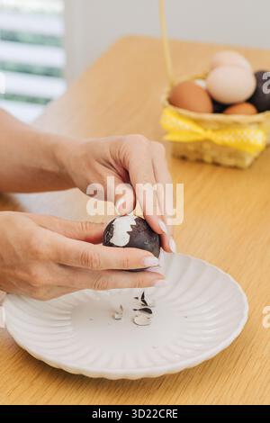 Una donna sbuccia un uovo di Pasqua a tavola. Buona Pasqua Foto Stock