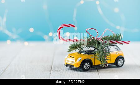 Auto giocattolo con ramo di abete e lecca-lecca su sfondo blu con luci natalizie Foto Stock