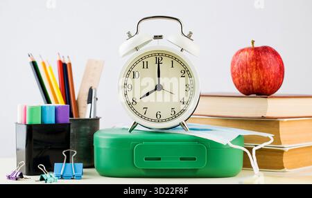 Torna a scuola. Una composizione di provviste scolastiche, una sveglia e una maschera protettiva. Foto di alta qualità Foto Stock