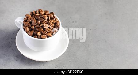 Chicchi di caffè arrosto in una tazza bianca su sfondo grigio. Foto Stock
