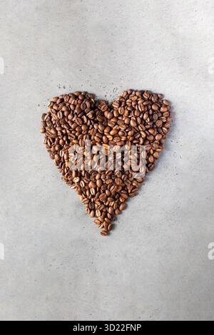 Chicchi di caffè a forma di cuore su sfondo grigio. Foto Stock