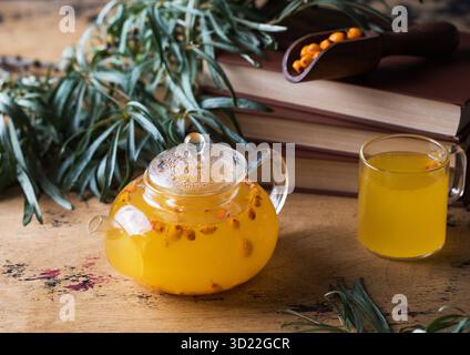 Teiera trasparente con tè alle fibbie di mare su sfondo ligneo. Tè d'autunno. Foto Stock