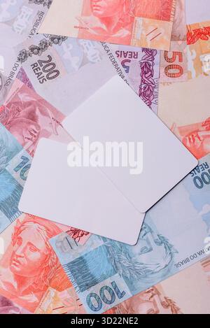 La carta di plastica bianca come simbolo dei pagamenti senza contanti sullo sfondo di denaro cartaceo del Brasile Foto Stock