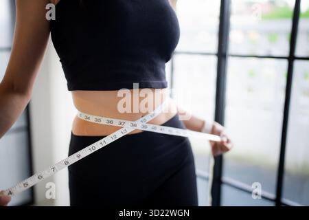 Asiatica donna sana dieta perdita di peso. Donna sottile che misura la vita con metro a nastro dopo la dieta per il controllo del peso a casa. Foto Stock