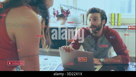 Collaborando alla scrivania, il marketer indossa la parte superiore rossa che punta verso un notebook aperto con sovrapposizioni fluttuanti Foto Stock