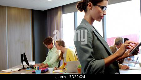 Donna in piedi con un blazer grigio che utilizza un tablet nella sala riunioni con un computer portatile in vaso, spazio per copiare Foto Stock