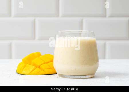 Frullato di mango rinfrescante in un bicchiere con mango a fette su sfondo chiaro Foto Stock