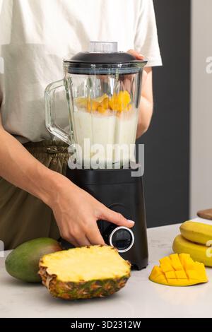 Preparazione di un frullato di ananas fresco al mango tropicale in un frullatore. Disintossicazione Foto Stock