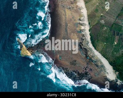 Vista aerea delle onde oceaniche che si infrangono contro una costa rocciosa e lussureggianti campi verdi. Lombok, Gerupuk, Indonesia Foto Stock