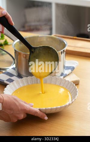La zuppa di zucca autunnale a base di ingredienti freschi viene versata in un piatto su un tavolo di legno. Foto Stock