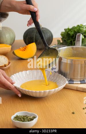 La zuppa di zucca autunnale a base di ingredienti freschi viene versata in un piatto su un tavolo di legno. Foto Stock