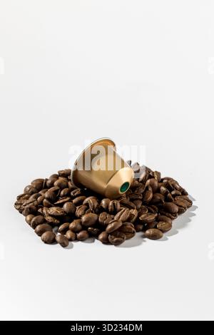 Capsula di caffè dorata sui chicchi di caffè su sfondo bianco. Pubblicità Foto Stock