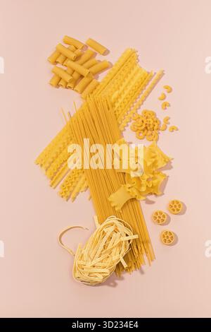 Varietà assortite di pasta cruda disposte su sfondo rosa, con forme diverse Foto Stock
