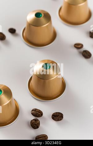 Capsule di caffè dorate e chicchi sparsi su sfondo bianco Foto Stock