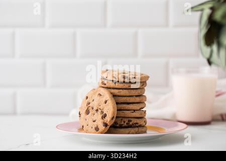 I biscotti vengono spalmati su un piatto, un bicchiere di latte fresco. Biscotti fatti in casa con gocce di cioccolato. Foto Stock