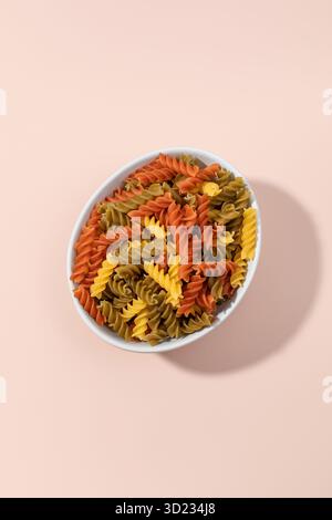Fusilli tricolori in una ciotola su sfondo rosa Foto Stock