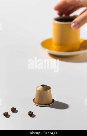 Capsula di caffè dorata e una tazza di caffè su sfondo bianco Foto Stock