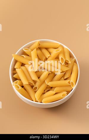 Penne crude in una ciotola su sfondo beige, cucina italiana. Foto Stock