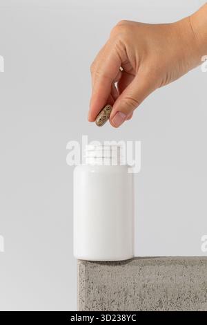 La mano di una donna toglie una pillola da un barattolo bianco. Preparazioni mediche. Foto Stock