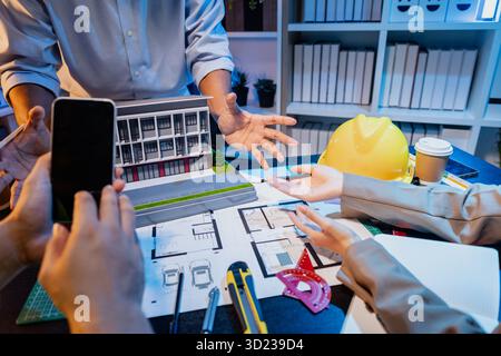 Un team diversificato di professionisti condivide idee su layout architettonici e concetti strutturali, concentrandosi sul lavoro di squadra, la creatività e la precisione in m Foto Stock