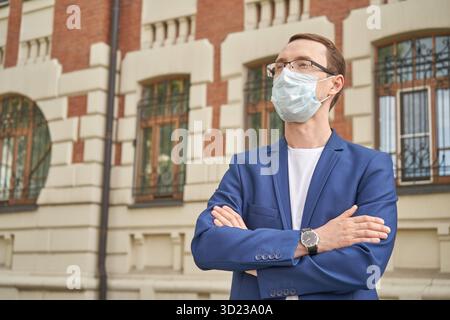 Uomo caucasico adulto in tuta blu che indossa la maschera in piedi con sicurezza all'aperto Foto Stock