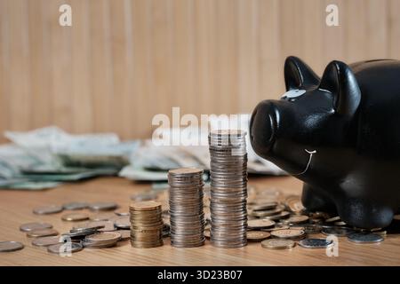 Il salvadanaio nero e le monete impilate simboleggiano il risparmio di denaro e la crescita finanziaria Foto Stock