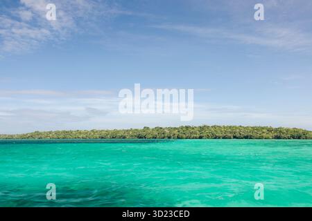 Vivace mare turchese con una densa isola verde sotto un cielo azzurro. Pulau Bair o Bair Island a Kei Kecil, Reggenza sud-orientale di Maluku, Maluku, Indonesia Foto Stock