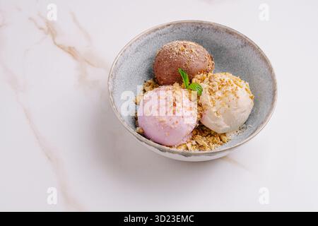 Tre palline di gelato colorato servite in una ciotola con noci tritate Foto Stock