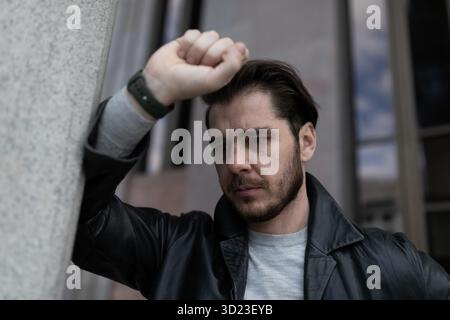 L'uomo barbuto in depressione si appoggia contro il muro esterno Foto Stock